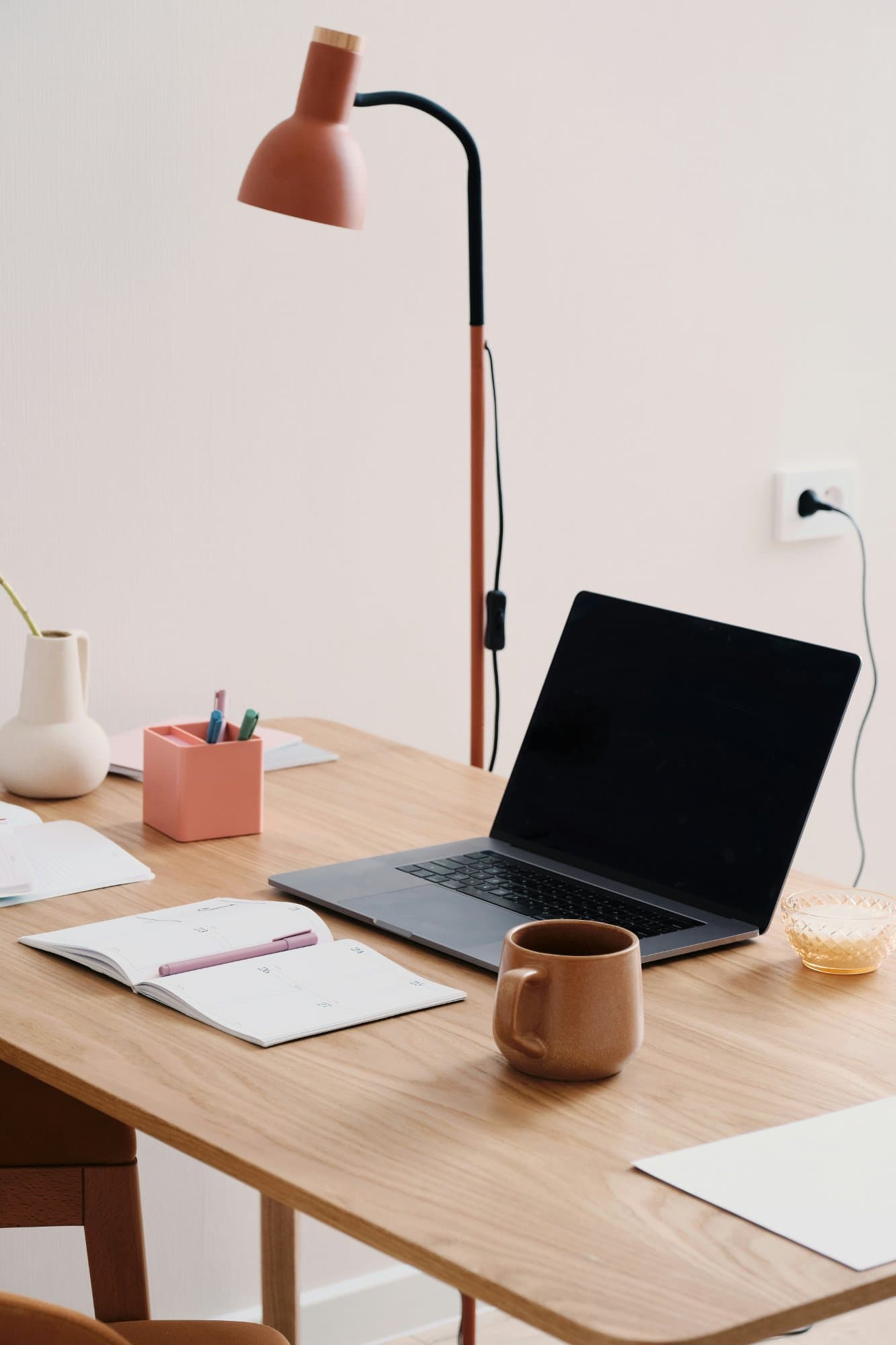 A tidy designer's desk with an open notebook, laptop, and coffee mug — warm wood tones and a calm workspace