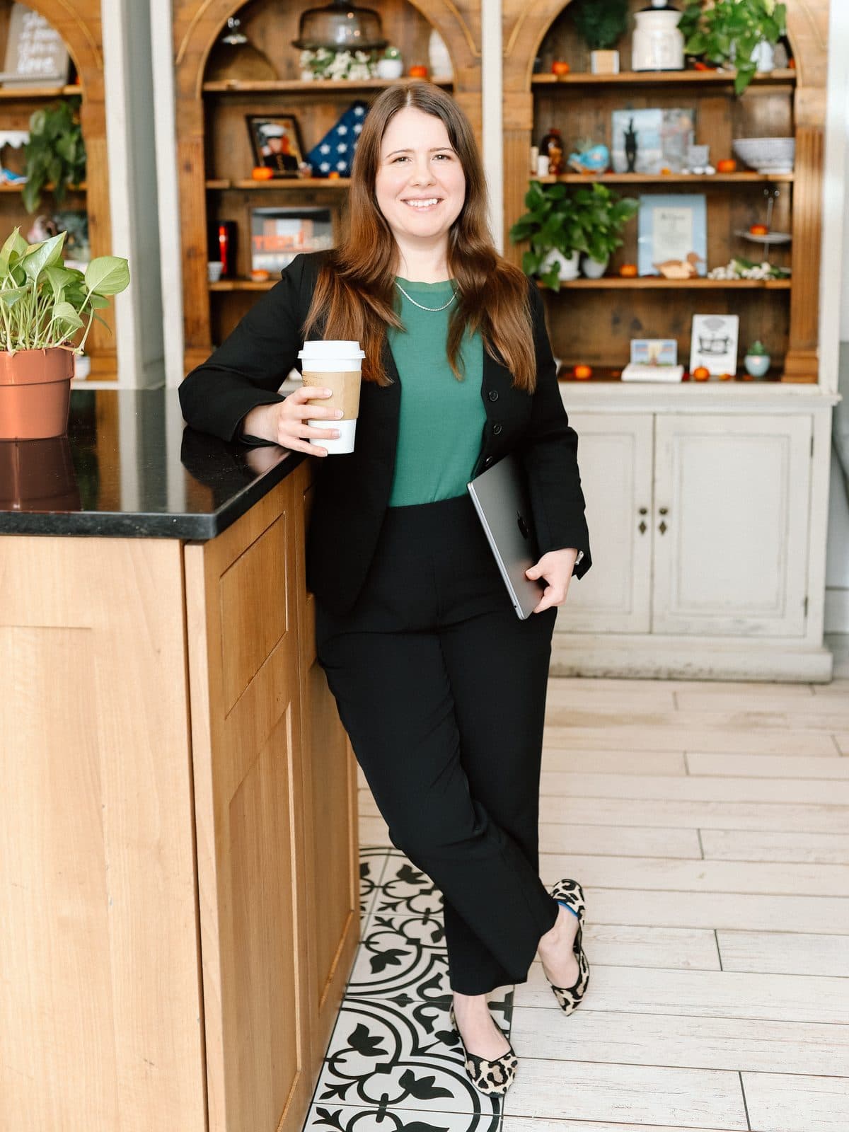 Jen Ross, founder of Mercury Jane, leaning on a coffee shop counter with a coffee in one hand and a laptop in the other