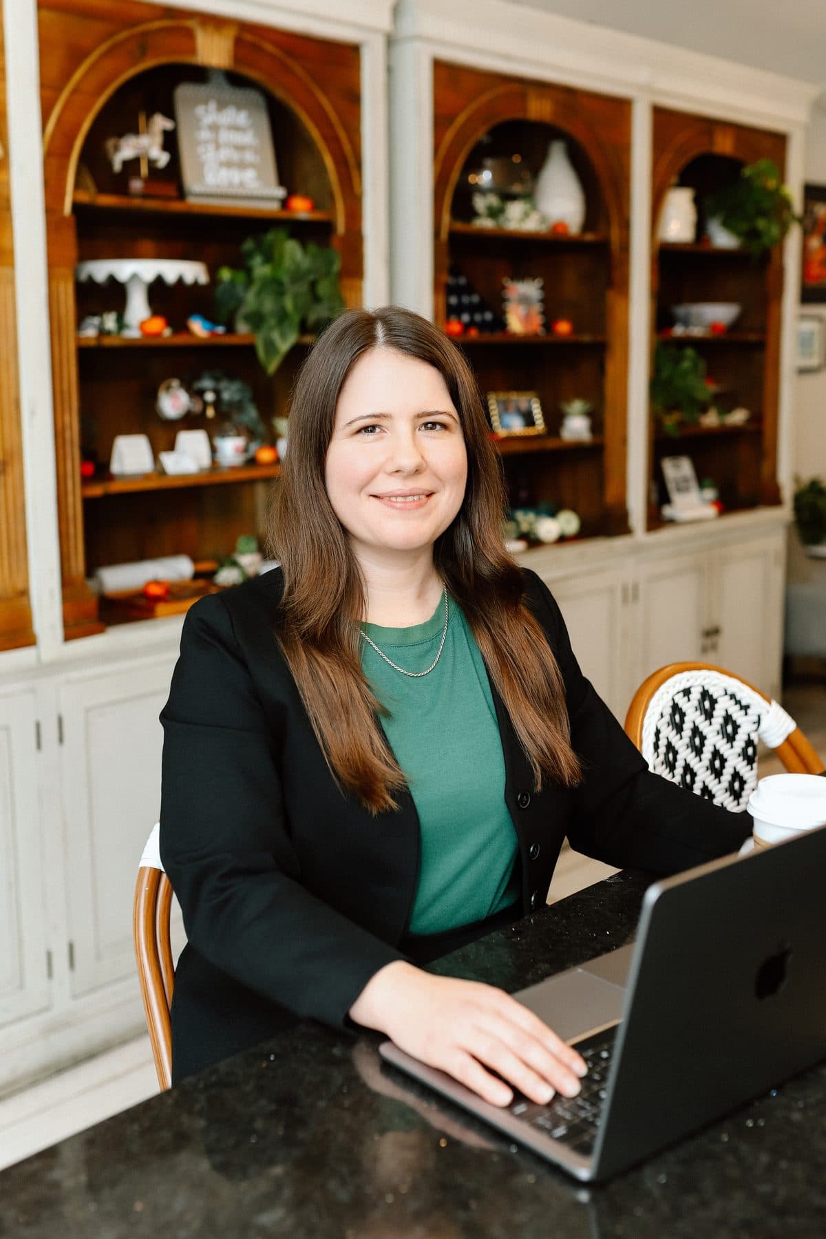 Jen Ross, founder of Mercury Jane, smiling at a coffee shop table with her hand on her laptop